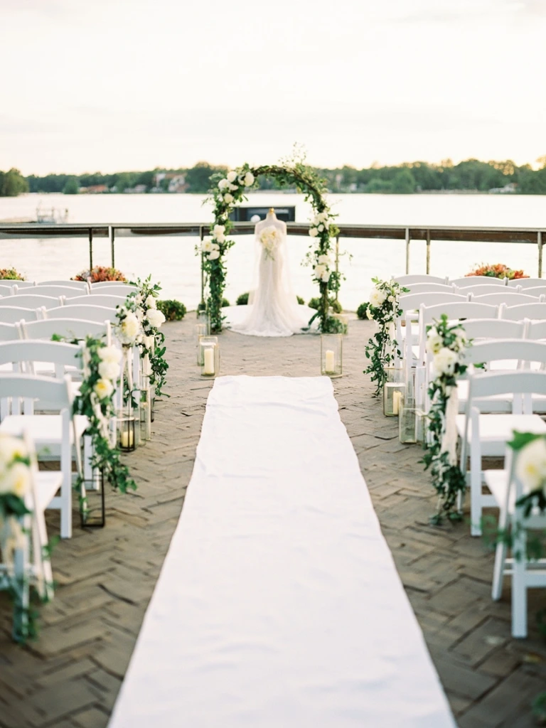 Ceremony aisle on the river deck with a floral arch of peonies and olive branches
